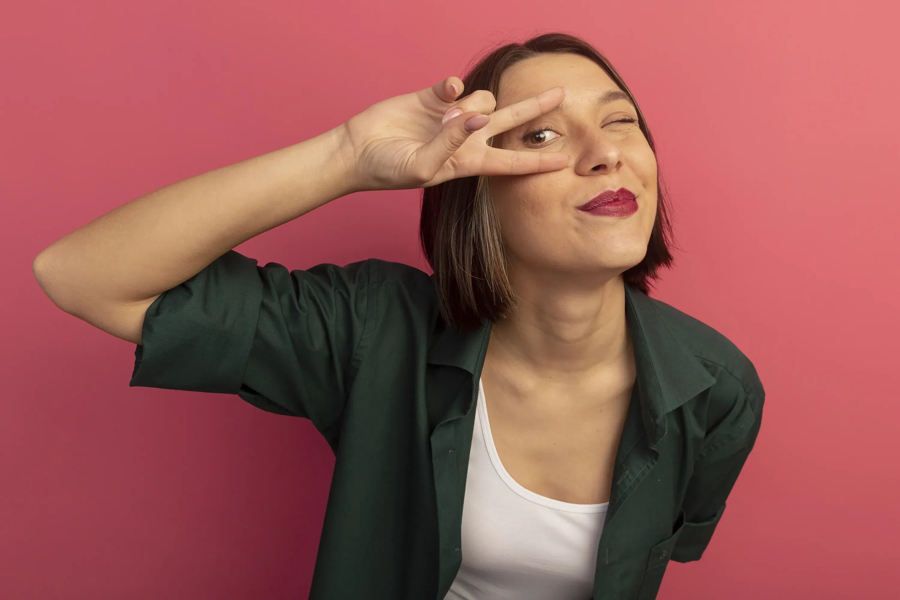 Confident woman over 40 showing eye area with a playful gesture against pink background